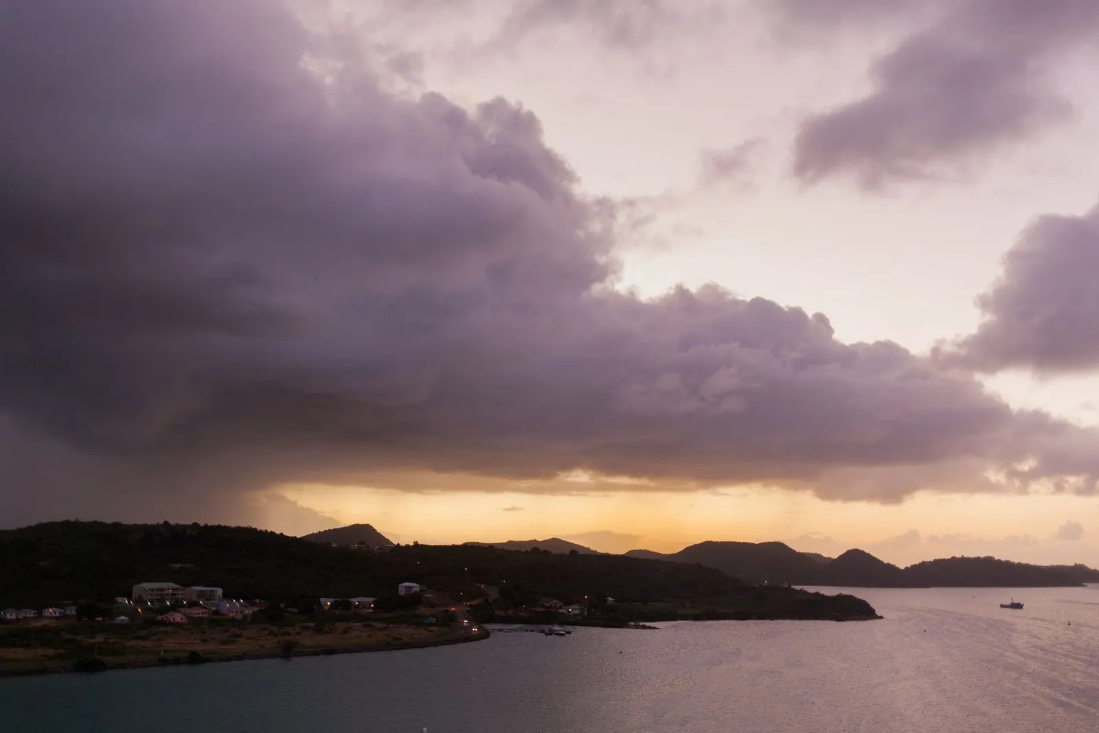 Dusk over a Caribbean coastline with hills and storm clouds at sunset