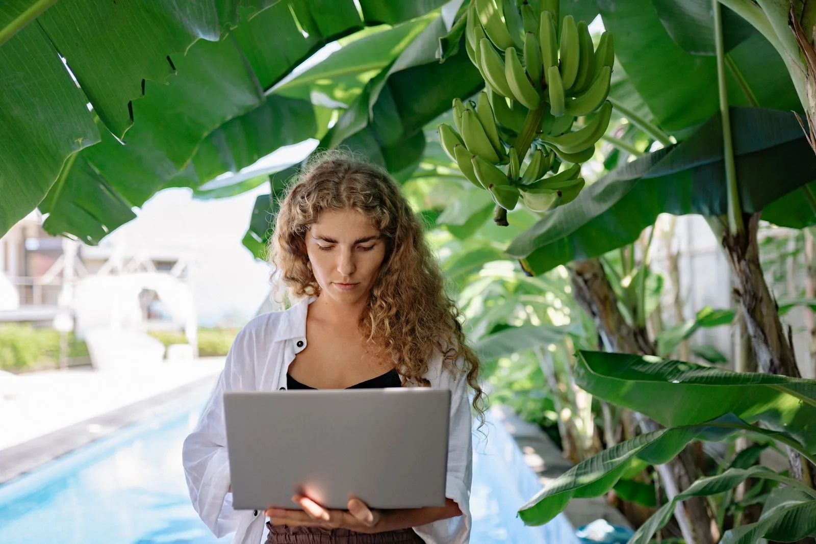 Woman working on a laptop under banana trees, the reality of digital nomad life in the Caribbean