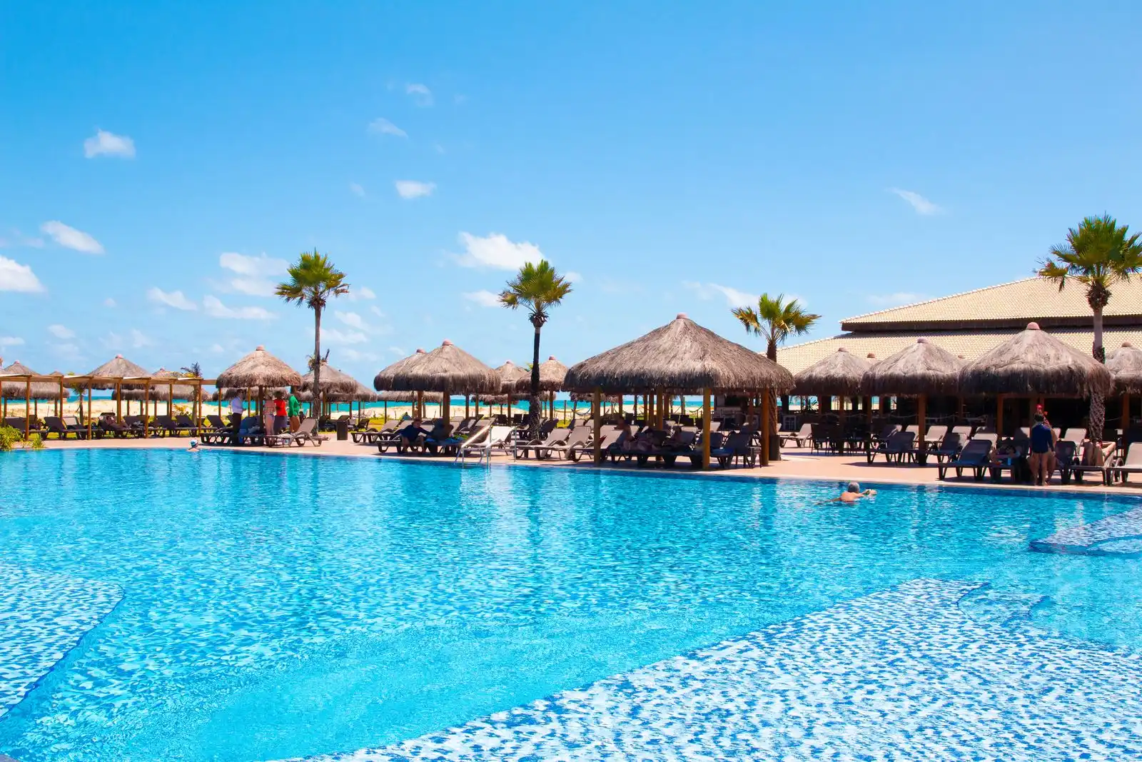 A tropical all inclusive resort pool with thatched shade huts